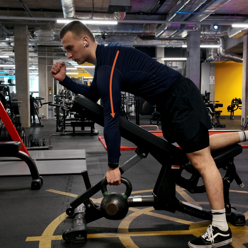 Wiosło z kettlebellem na ławce skośnej — pozycja wyjściowa, łopatka opuszczona, zaznaczona linia ruchu