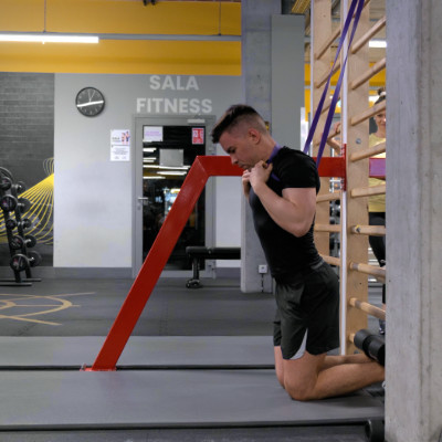 Nordic hamstring z asystą gumy — pozycja startowa: klęczenie ,guma zaczepiona o barki