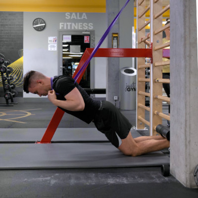 Nordic hamstring z asystą gumy — faza ekscentryczna: tułów kontrolowanie opada do przodu